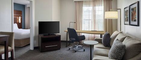 A hotel room with a bed, a desk, a television, a sofa, and a lamp.