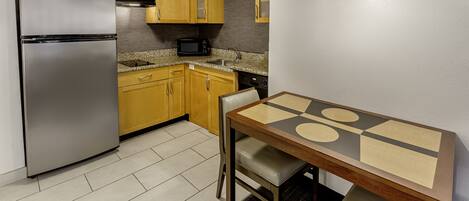 Una cocina compacta con armarios de madera, un refrigerador de acero inoxidable, un microondas y una mesa de comedor con sillas.