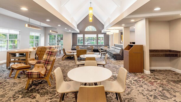 Un espace intérieur vaste et bien aménagé, avec différents types de sièges, notamment des tables rondes et des bancs rembourrés, ainsi qu’une grande fenêtre offrant une vue sur l’extérieur.