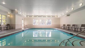 Une piscine intérieure à l’eau claire, entourée de chaises et dotée d’une fenêtre laissant entrer la lumière naturelle.