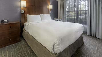 Une chambre d’hôtel avec un grand lit, une tête de lit en bois, deux lampes de chevet, une petite table et une fenêtre avec des rideaux.