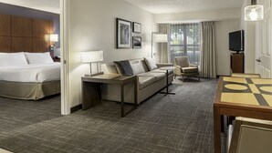 Une chambre d’hôtel avec un lit, un canapé, une petite table, une télévision et une fenêtre avec des rideaux.