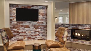 A modern living room with a fireplace, two leather armchairs, and a flat-screen TV mounted on a brick-patterned wall. - Residence Inn by Marriott Scranton (Scranton)