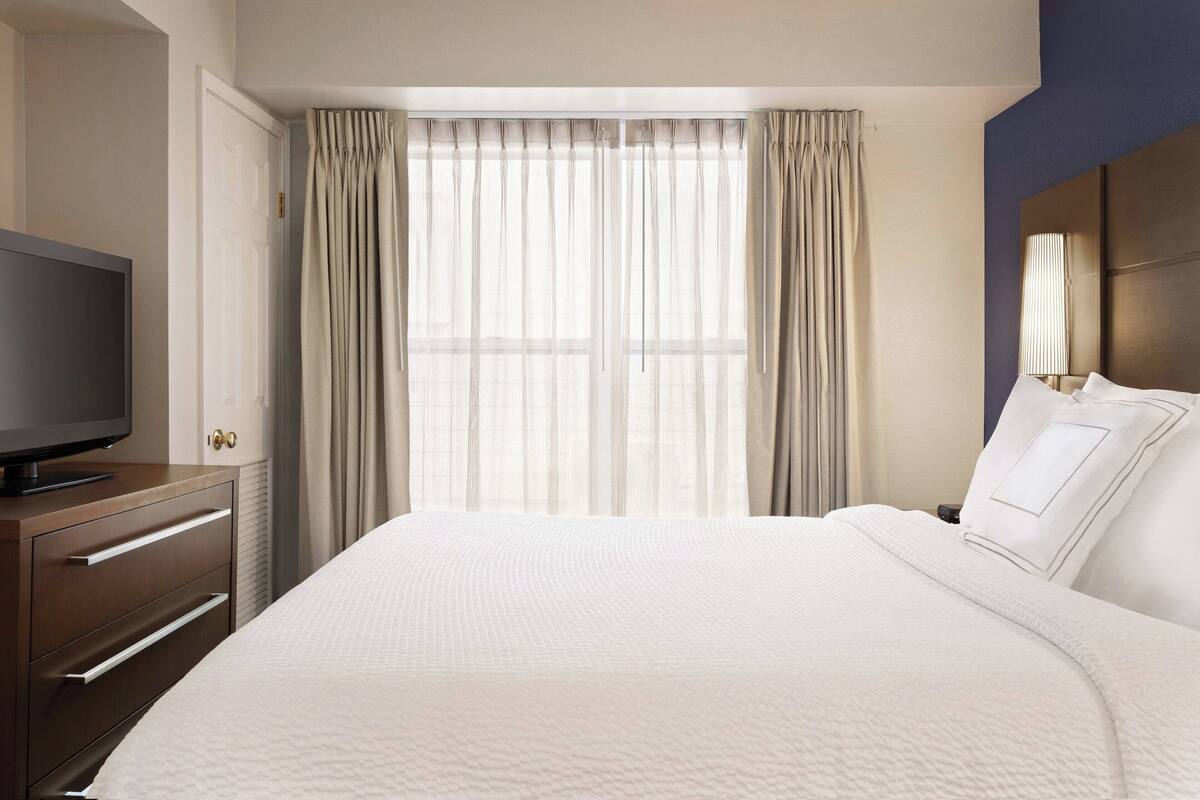 A hotel room with a large bed, a television on a wooden dresser, and a window with curtains.