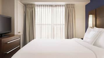 Une chambre d’hôtel avec un grand lit, un téléviseur posé sur une commode en bois et une fenêtre avec des rideaux.