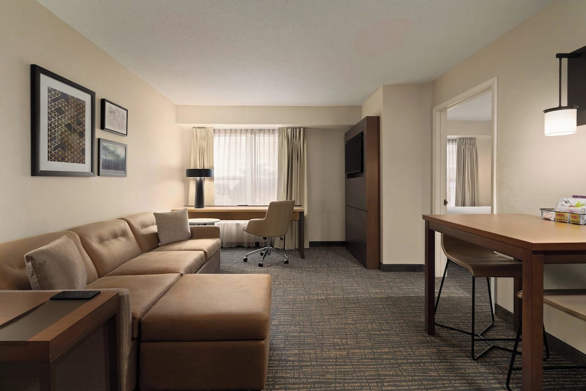 A hotel room with a sofa, a desk, a chair, a TV, and a lamp.