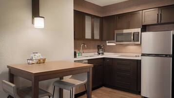 A modern kitchen with dark wooden cabinets, a stainless steel refrigerator, a microwave, and a coffee maker.