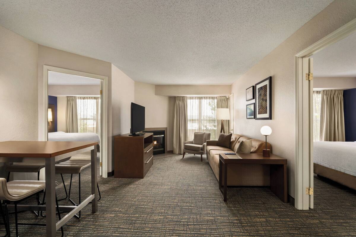 A hotel room with a bed, a sofa, a desk, a TV, and a fireplace.