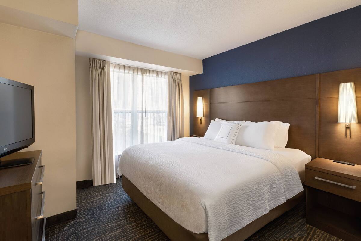 A hotel room with a large bed, a television, a nightstand, and a window with curtains.