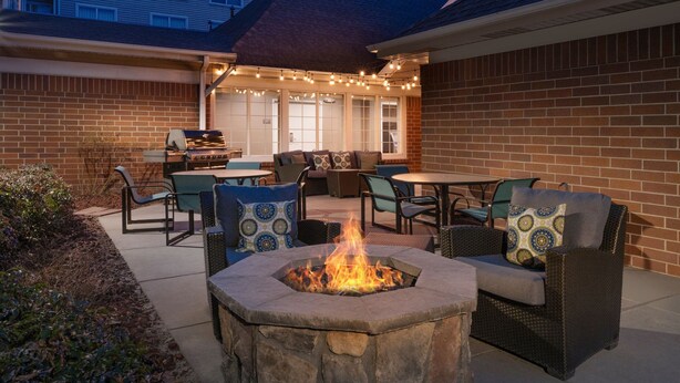 An outdoor patio area with a stone fire pit, wicker furniture, and string lights.