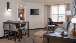 A hotel room with a dining area, a sofa, a TV, and a window with curtains.