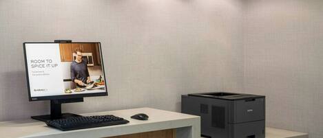A modern office space with a wooden desk, a computer monitor displaying a room setup, and a printer.