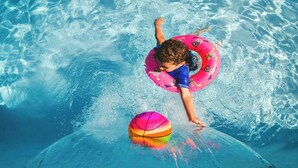Ein Kind im Schwimmbecken mit einem rosa Schwimmreifen und einem bunten Ball.