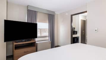 Una habitación de hotel con una cama grande, un televisor de pantalla plana sobre un soporte de madera, una ventana con cortinas y una puerta que da a un baño.