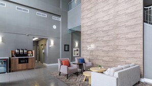 Eine geräumige Lobby mit modernem Design, ausgestattet mit einer Sitzecke mit Sofas und Sesseln, einer Kaffeestation und einer großen Holzwand als Blickfang.
