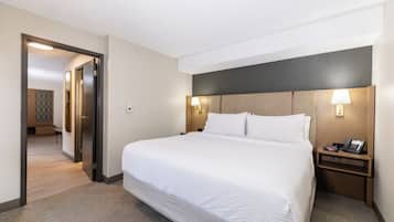 Et hotelværelse med en stor seng, et sengebord med lampe og en dør til et andet rum.