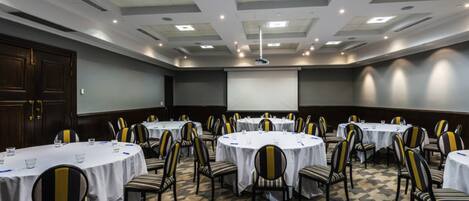 A conference room with multiple round tables, chairs, and a projector screen.
