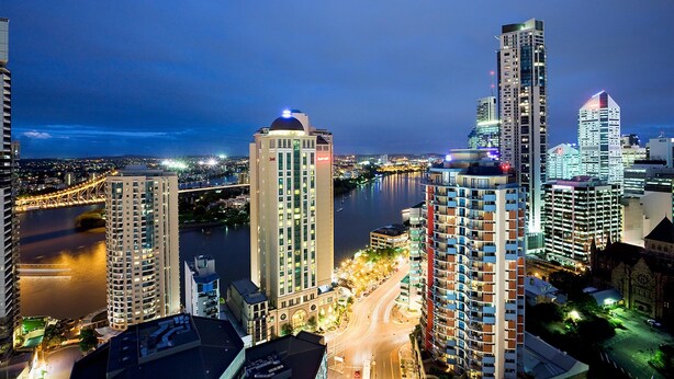 A cityscape at night with high-rise buildings, a river, and a bridge. - Mantra on Queen (Brisbane)