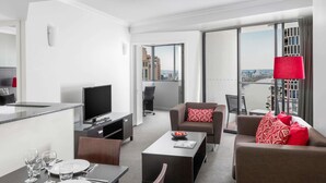 A modern hotel room with a dining area, a TV, a sofa, and a view of the city. - Mantra on Queen (Brisbane)
