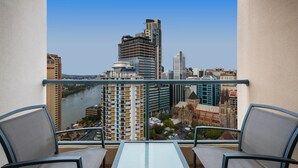 A balcony with two chairs and a table, overlooking a cityscape with a river and various buildings. - Mantra on Queen (Brisbane)