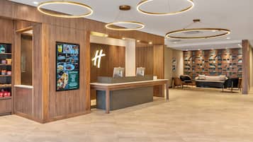 A reception area with a wooden reception desk, a large illuminated 'H' sign, and a seating area with a patterned wall and a sofa.