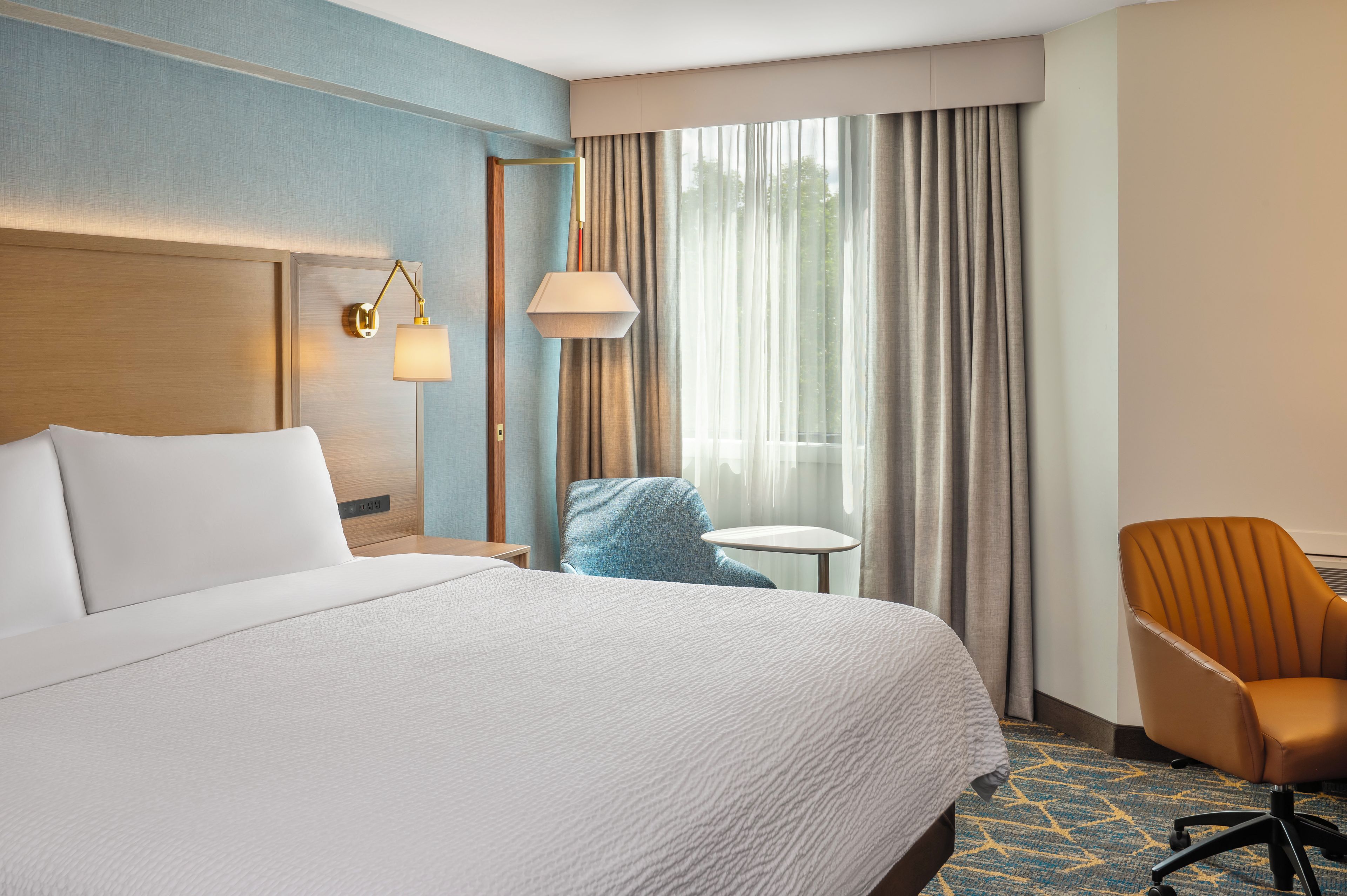 A hotel room with a large bed, a desk, a chair, and a window with curtains.