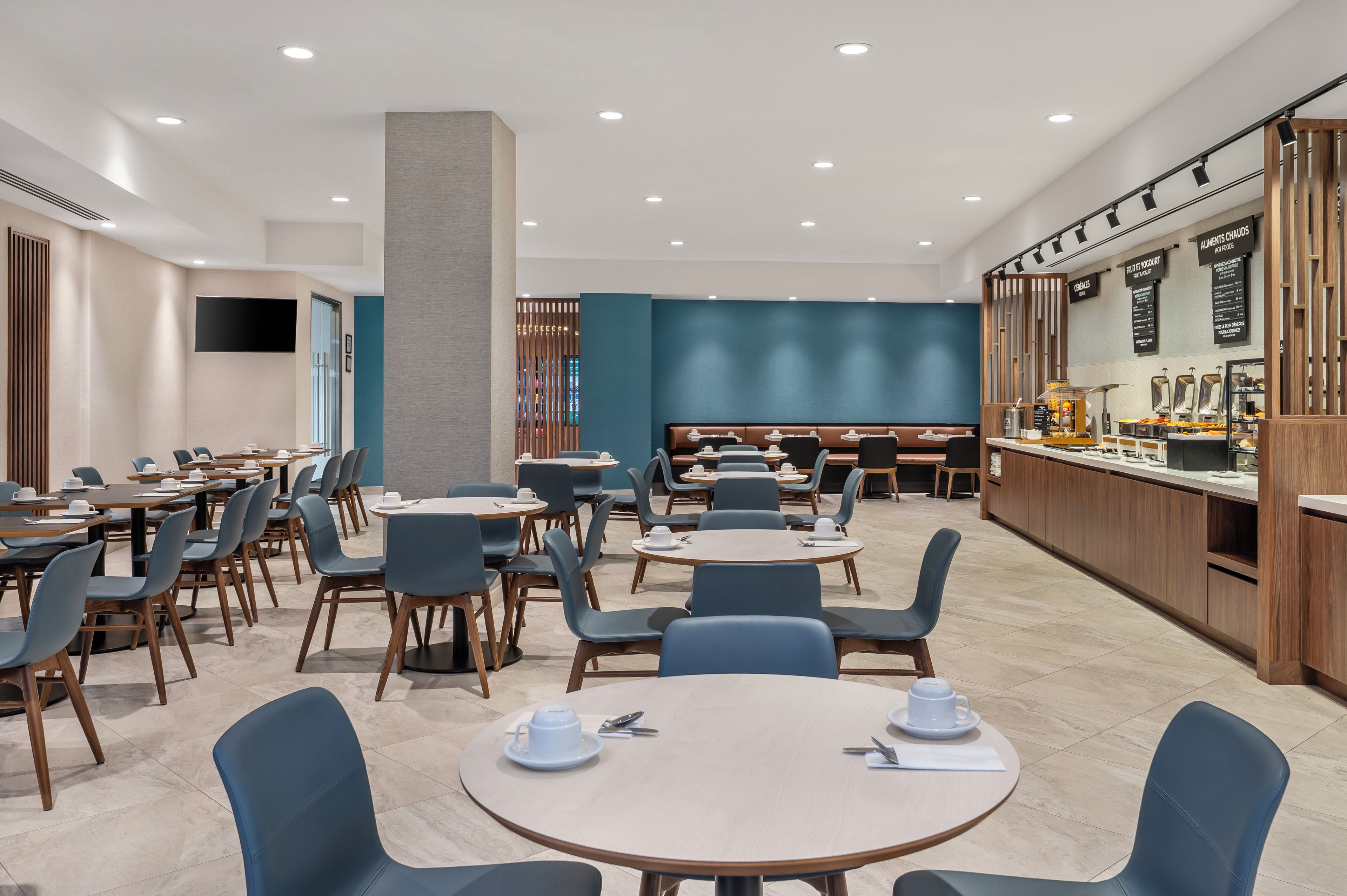 A modern dining area with round tables and blue chairs, a central pillar, and a food display counter.