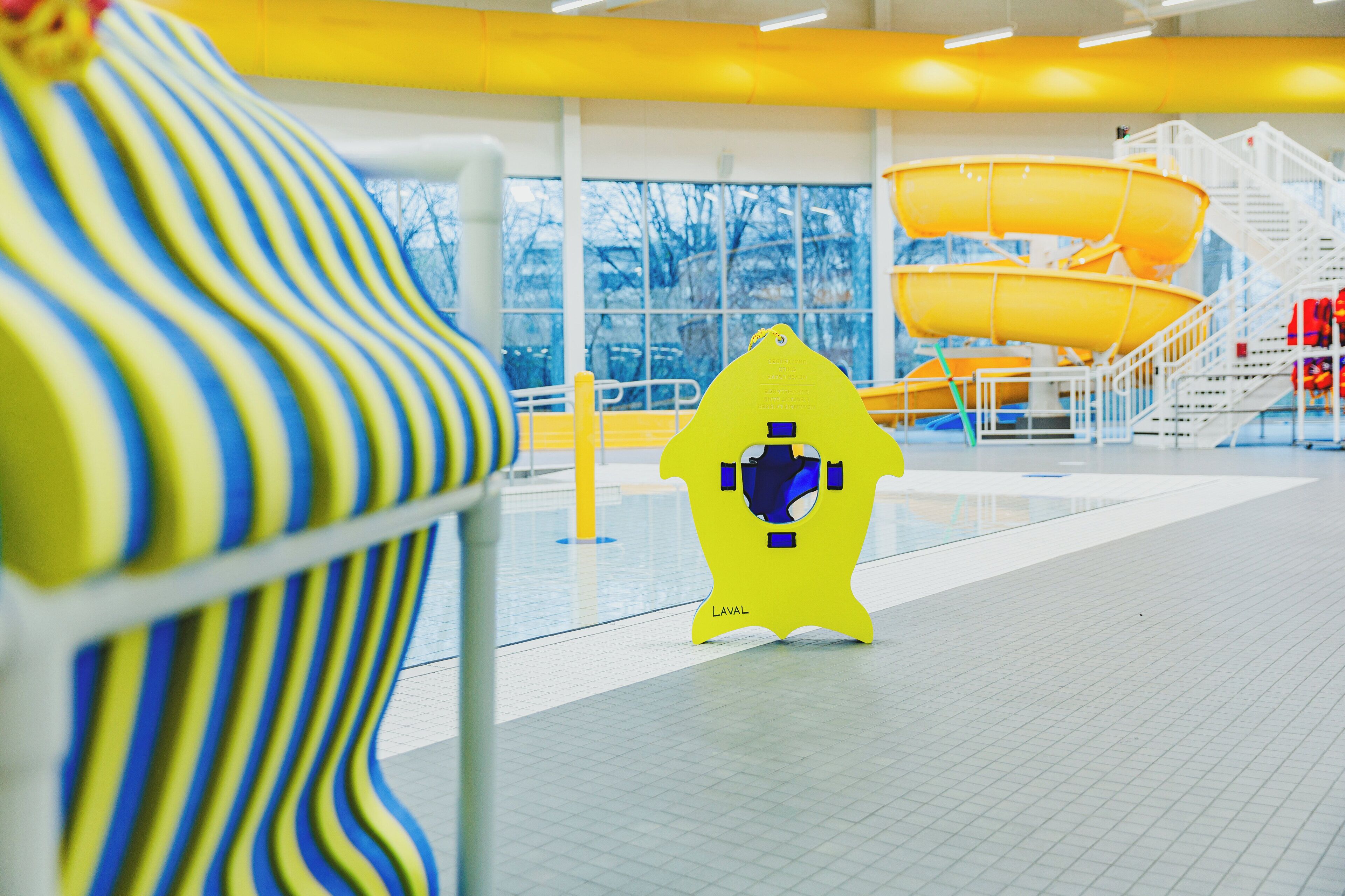 Una torre amarilla de salvavidas, un tobogán amarillo y una silla a rayas en una zona de piscina.