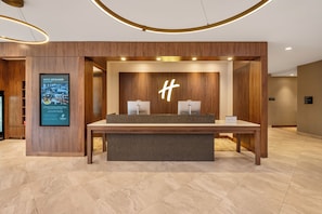 Una recepción con detalles de madera, un gran letrero iluminado con la letra 'H' y una pantalla digital mostrando información del hotel.