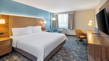 Una habitación de hotel con una cama grande, un escritorio, una silla, un televisor y un ventanal con cortinas.