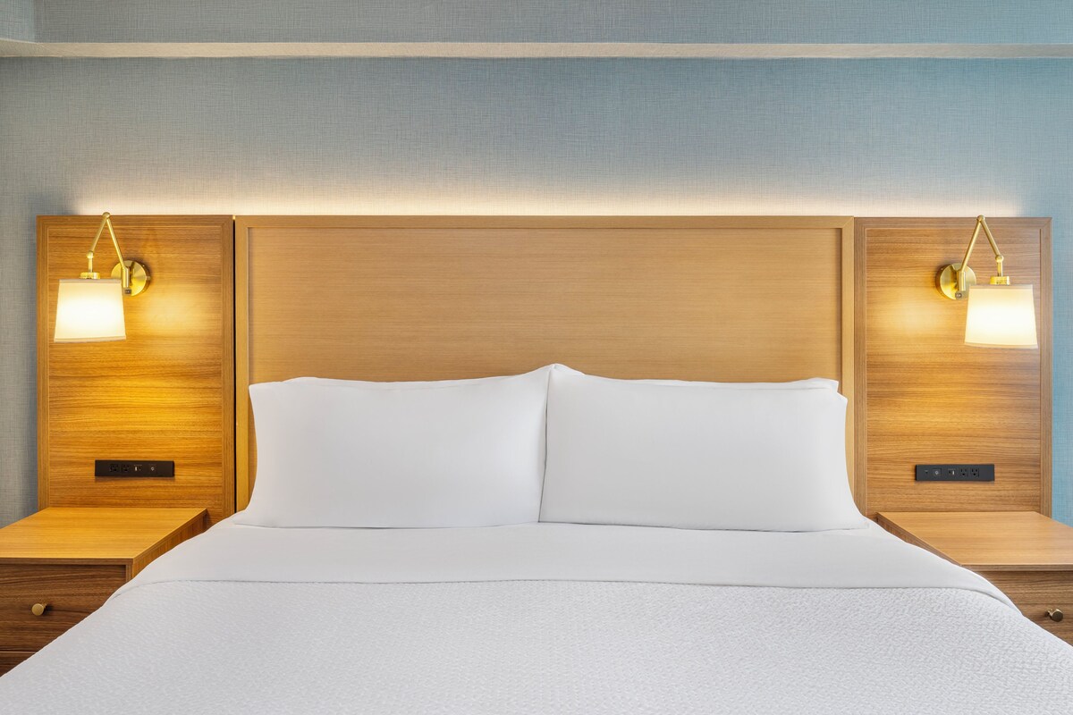 Una habitación de hotel con una cama grande, dos mesitas de noche y lámparas fijadas a la pared.