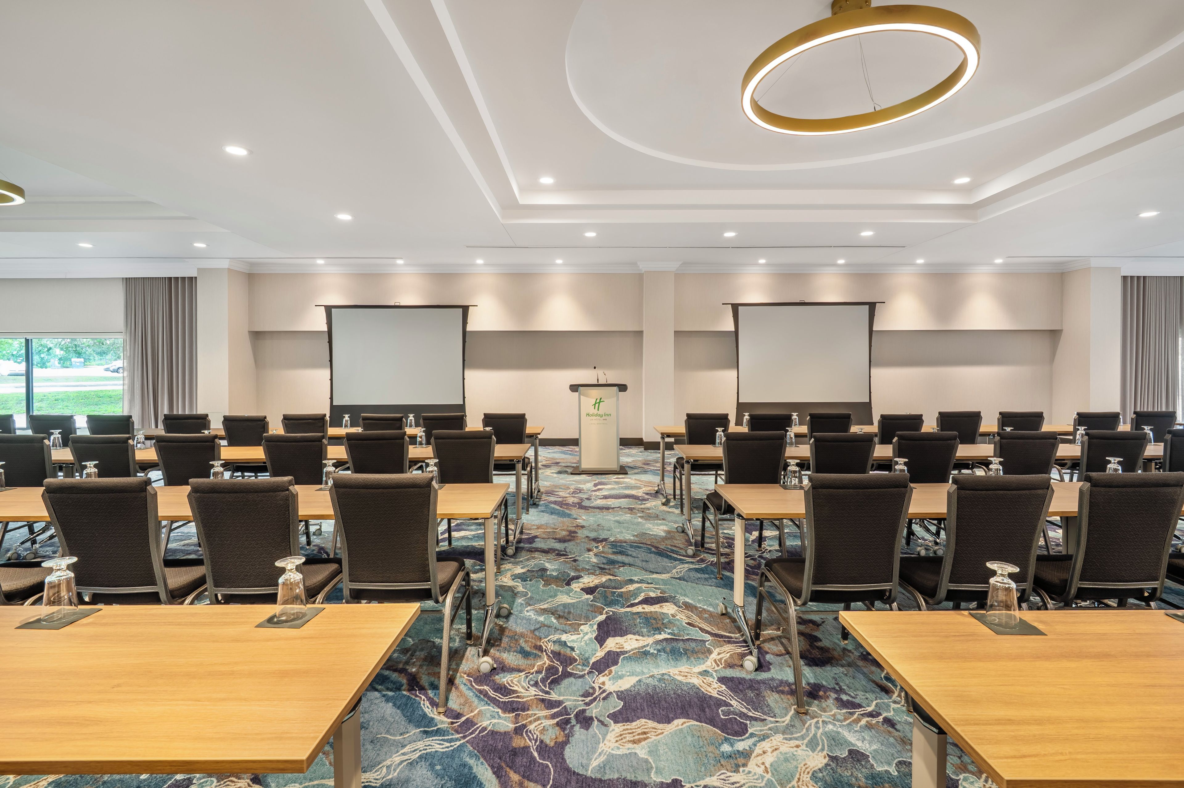 A conference room with multiple tables and chairs, a carpeted floor, and a large screen at the front.