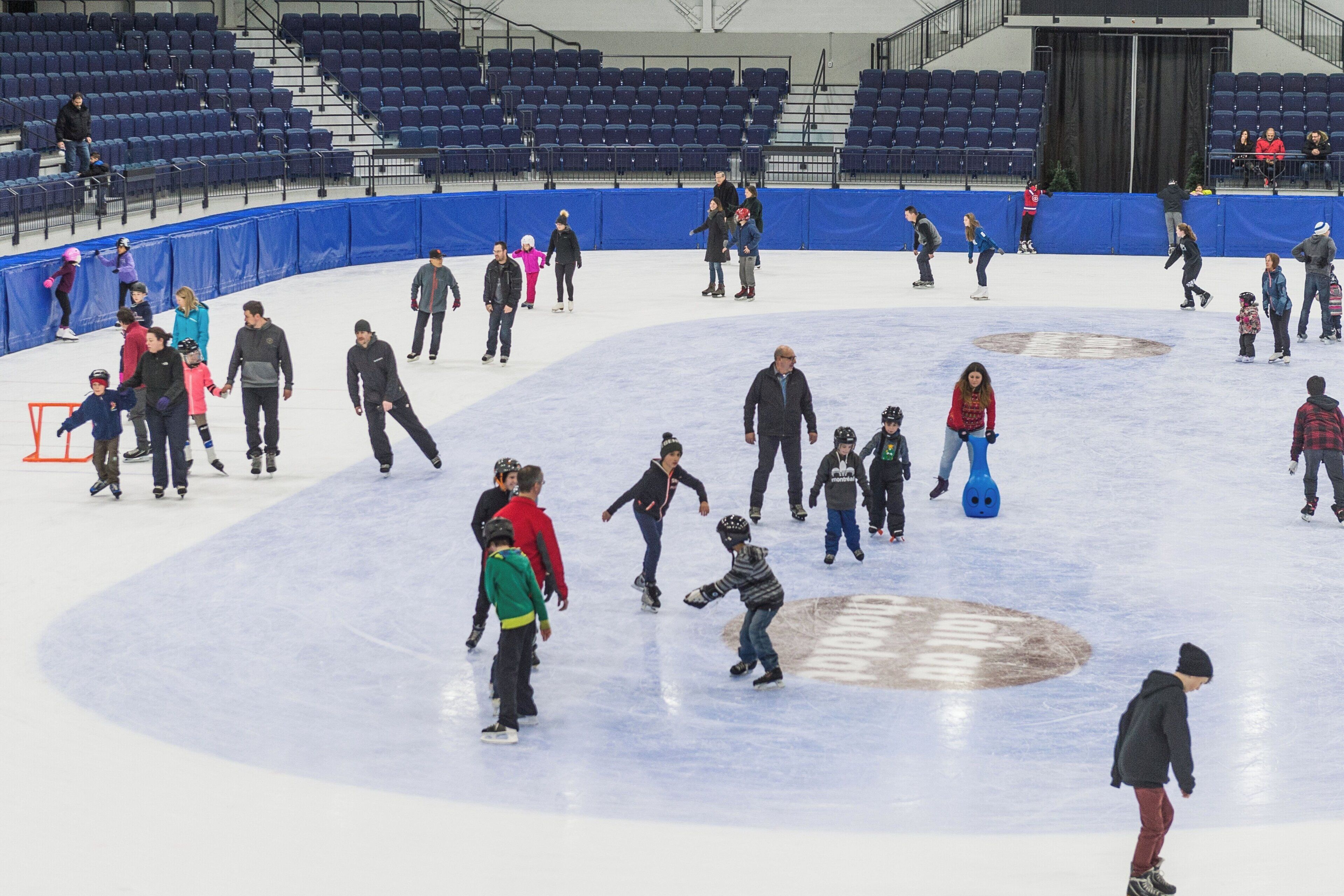 An indoor ice skating rink with people skating and standing around.