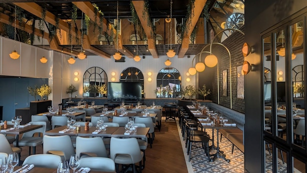Ein Restaurant mit mehreren Tischen, Stühlen, einem großen Fernsehbildschirm und hängenden Pflanzen.