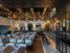 A restaurant with multiple dining tables and chairs, a large TV screen, and hanging plants. - Holiday Inn Laval Montréal by IHG (Laval)