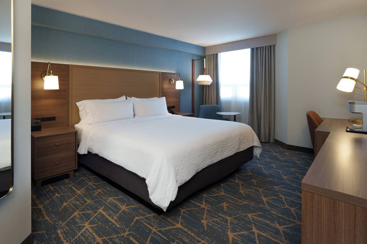 A hotel room with a large bed, a desk, two bedside tables, and a chair.