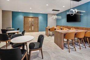 Un salón de conferencias con una mesa y sillas de madera, una pantalla grande y una pared azul de acento.