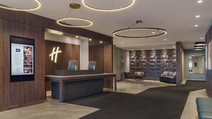Ein moderner Empfangsbereich mit einem Holzbüro, dem großen 'H'-Logo und einer Sitzecke mit einem gemusterten Wandbild.