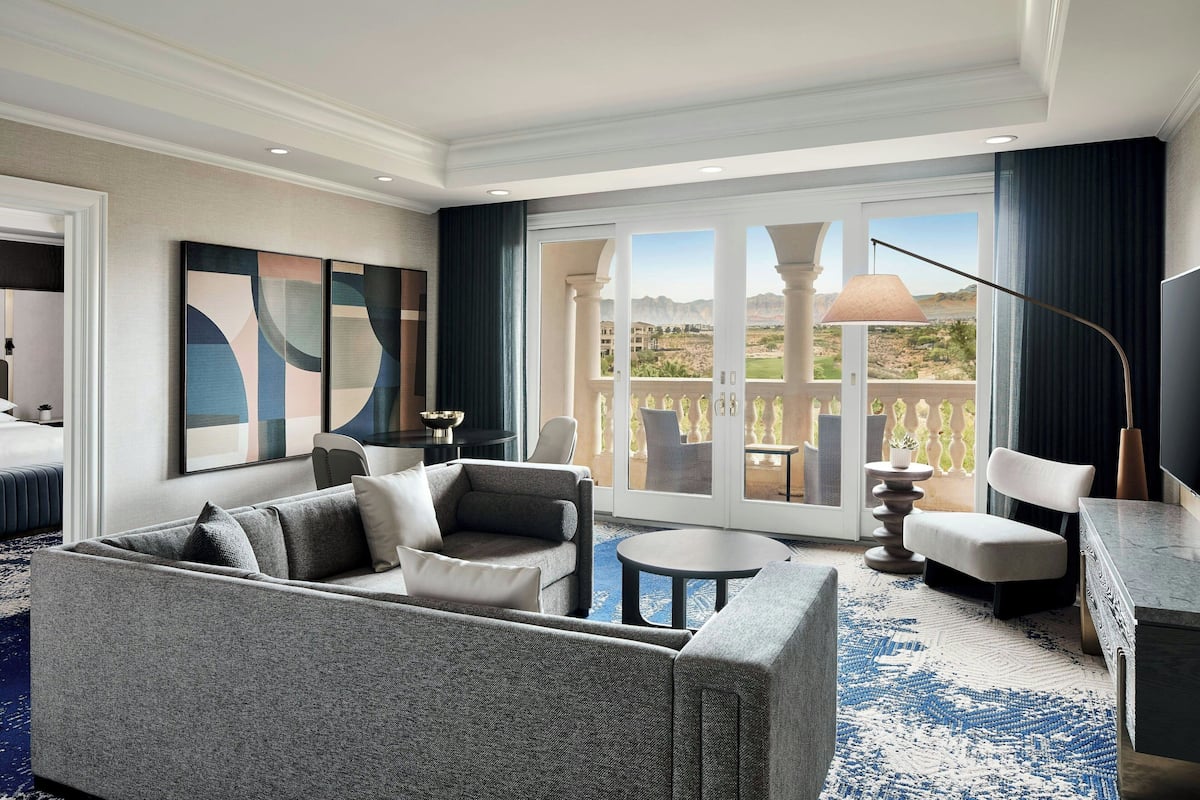 A modern hotel room with a grey sofa, a round coffee table, and a view of the desert through large sliding doors.