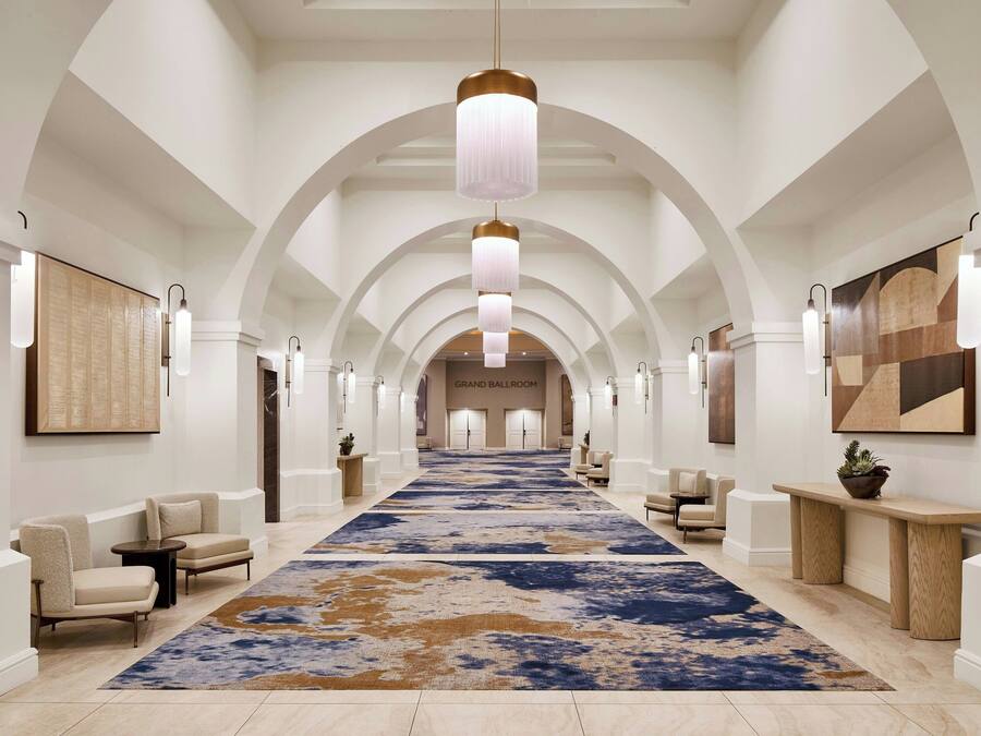 A hotel lobby with a long corridor, arched ceiling, and a large blue and brown patterned carpet.