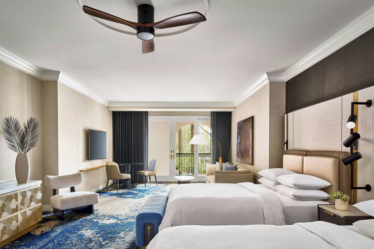 A hotel room with a large bed, a desk, a chair, a sofa, a TV, and a balcony with a view.