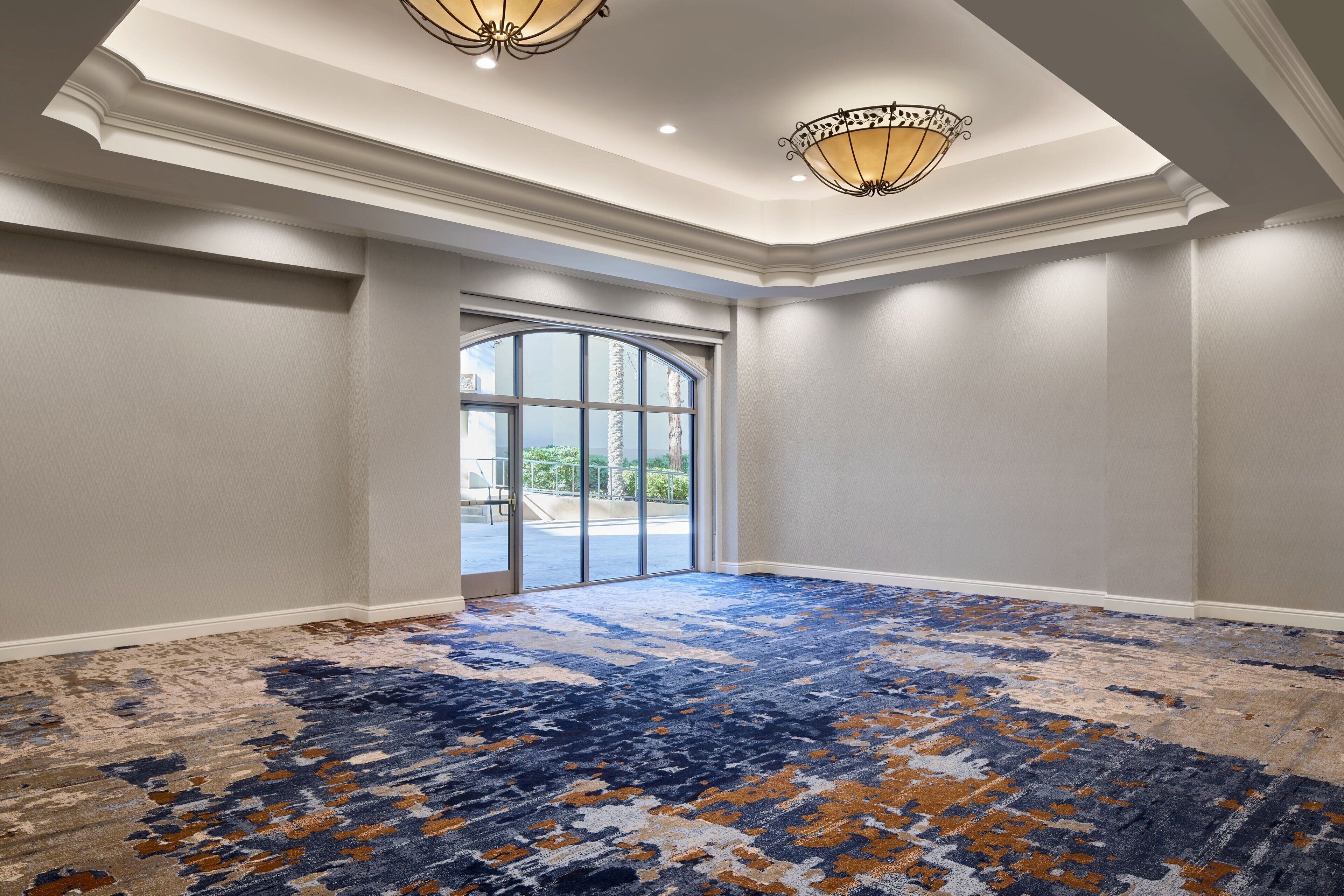 A spacious room with a large window, a patterned carpet, and a chandelier.