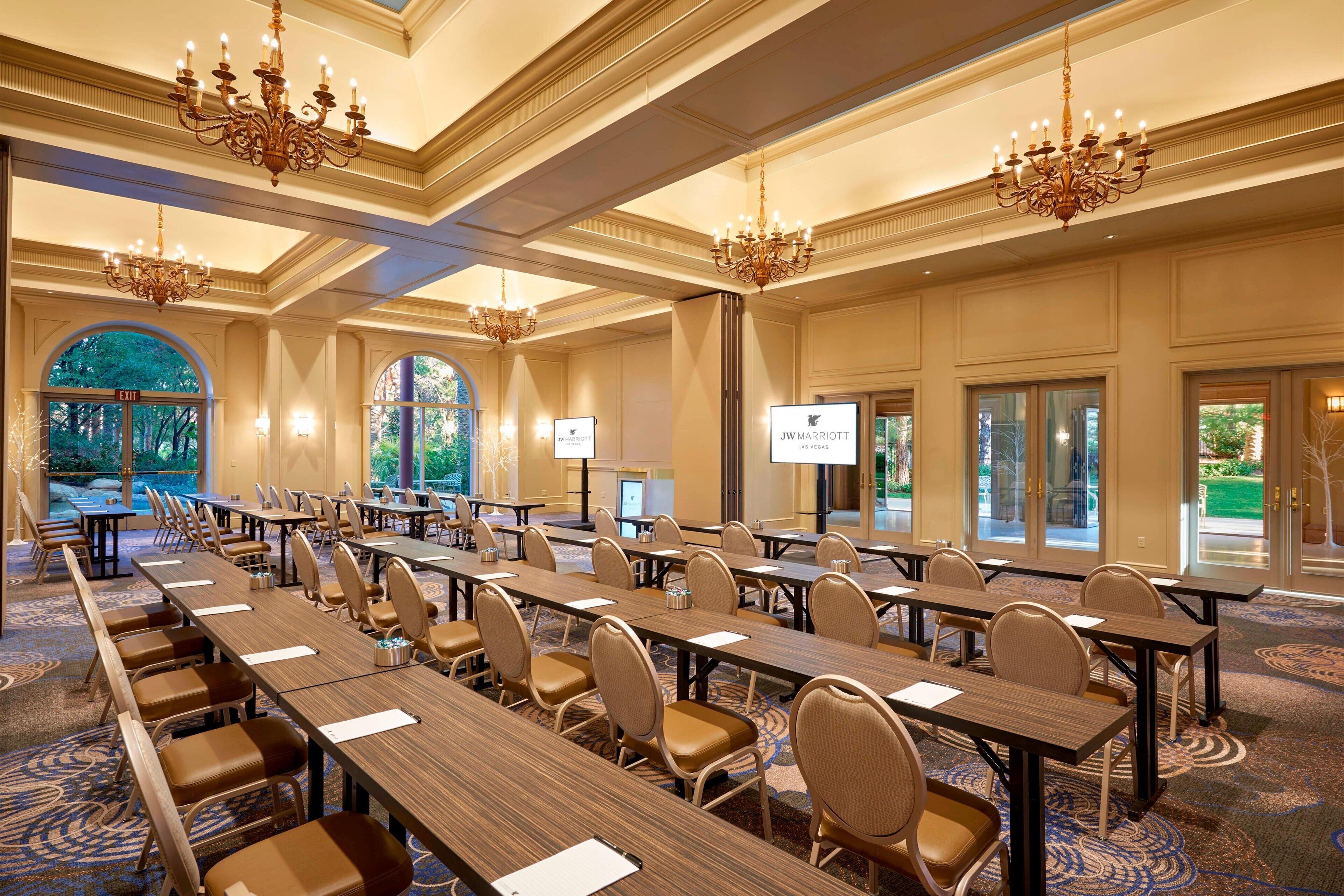 A conference room with long tables, chairs, chandeliers, and large windows.