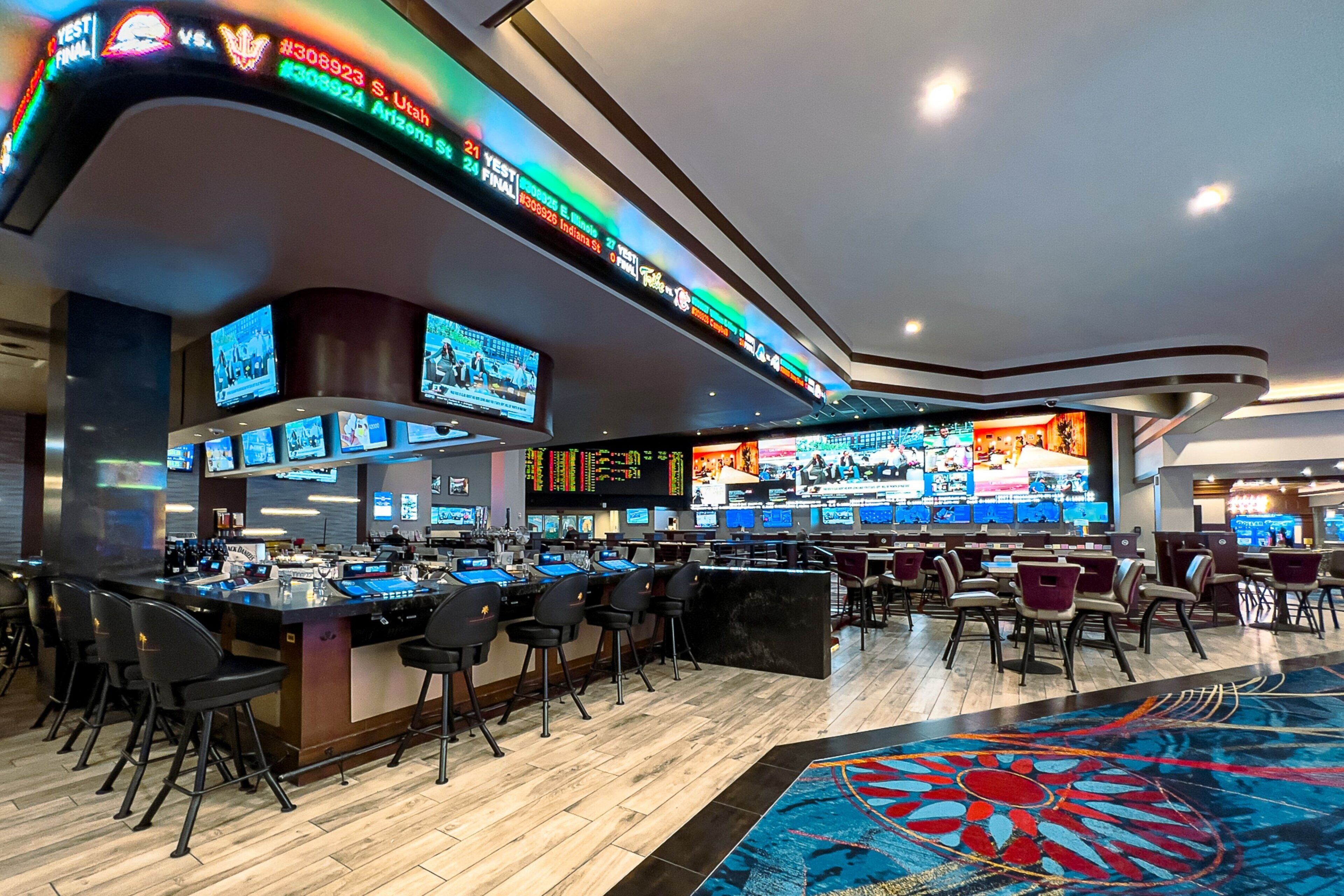 A casino bar with multiple screens, bar stools, and a patterned carpet.