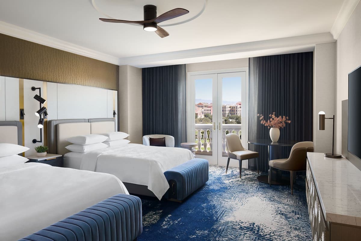 A hotel room with two beds, a seating area, a balcony with a view, and a TV.