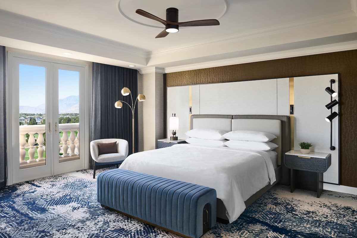 A hotel room with a large bed, a bench, a chair, a nightstand, and a view of the outdoors.