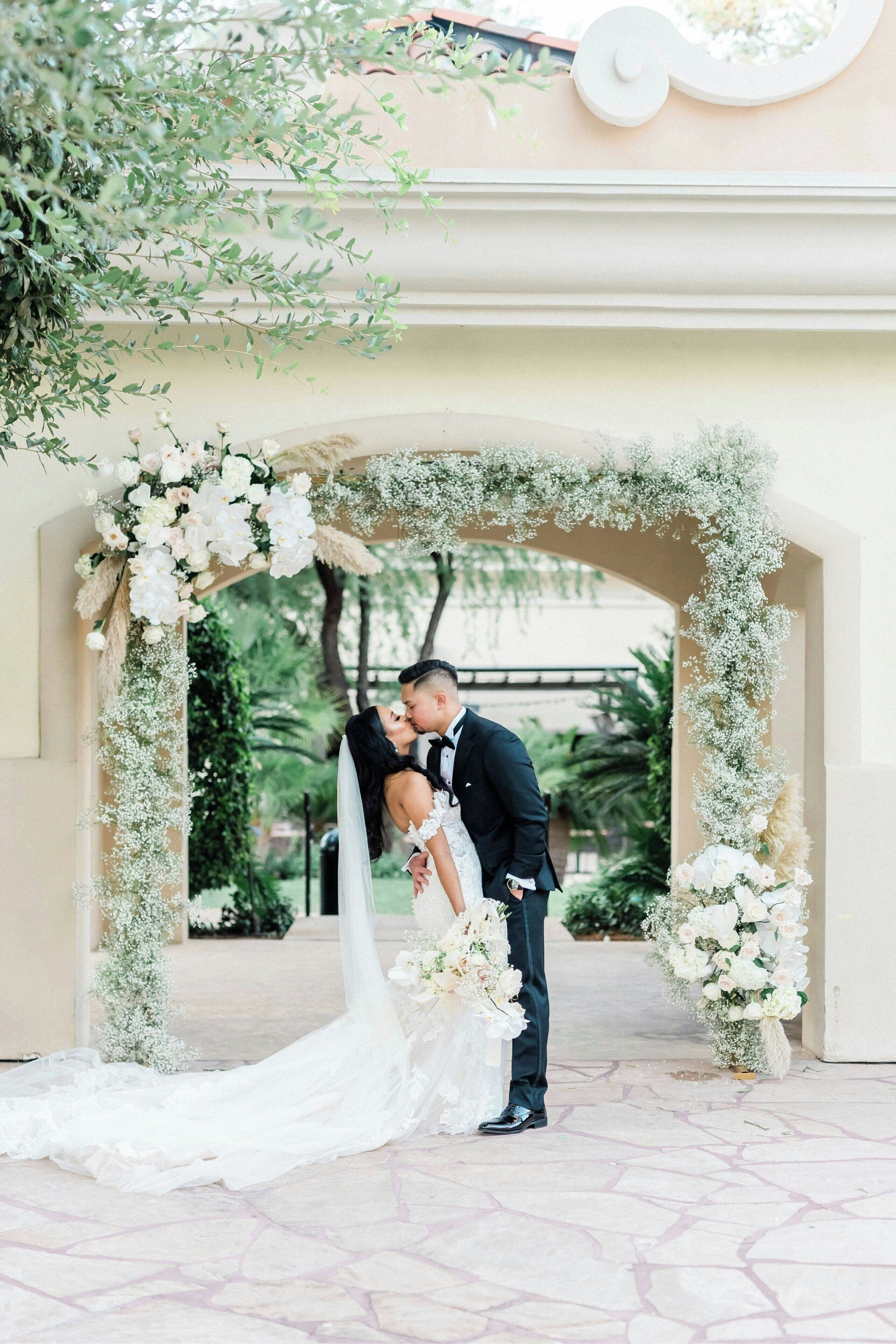 Una ceremonia de boda bajo un arco floral ornamentado con follaje y flores.