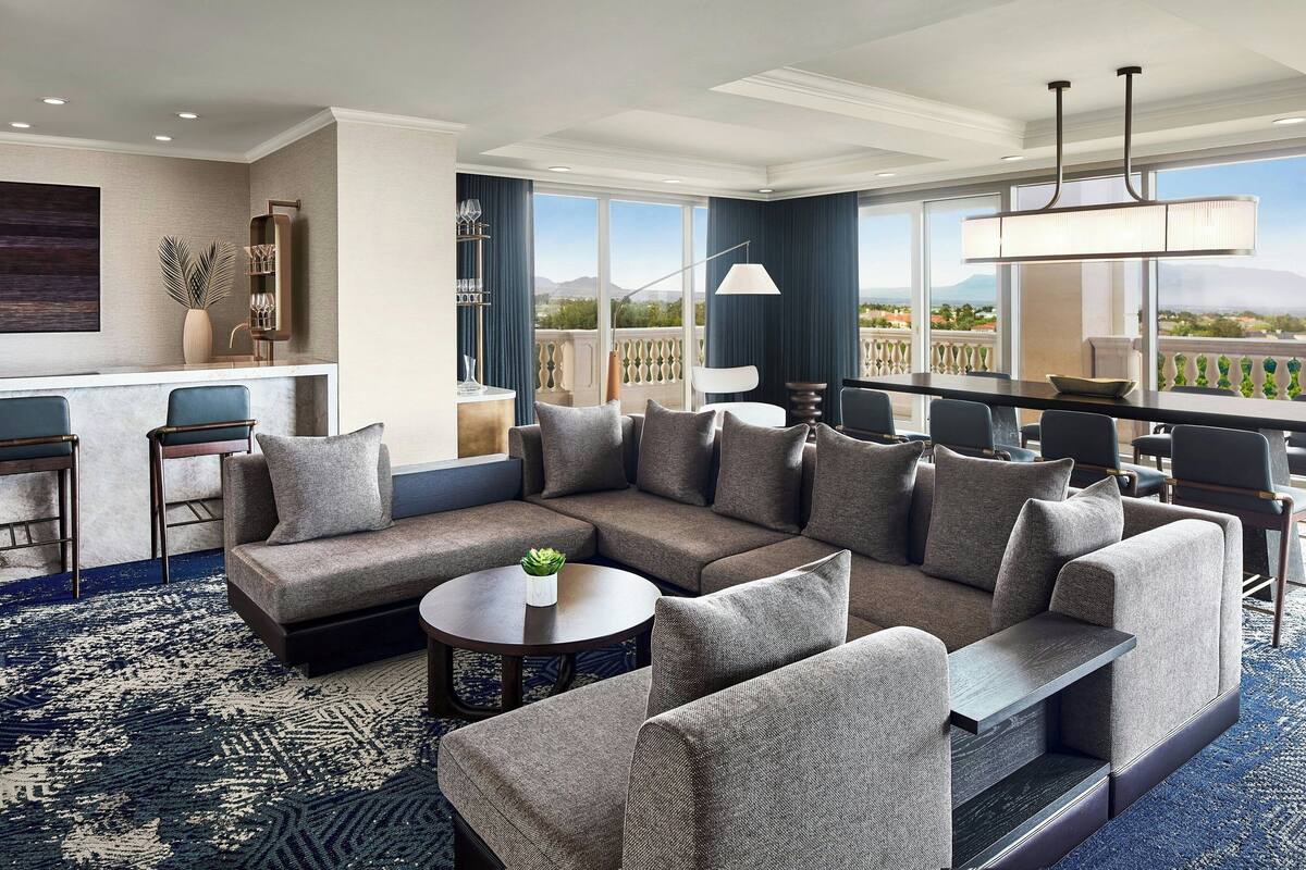 A modern hotel lobby with a large sectional sofa, a round coffee table, and a bar area.