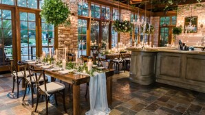 A rustic dining area with wooden tables, chairs, and hanging greenery.