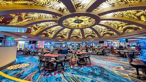 A casino interior with a patterned carpet, gaming tables, and a ceiling with leaf-like designs.